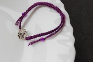 pulsera trenzada púrpura con chakra sahasrara en el borde de un plato blanco como la nieve
