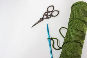 Blue crochet hook and a skein of cord on a white background. On one hook - a loop from the cord, made to start knitting. Vintage scissors are nearby