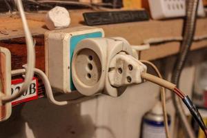 An old electric plug with a rewound electrical tape plugged into a socket. Electrical wiring in the garage photo