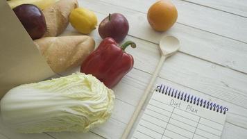 Full paper bag of food products with blank little notebook on wooden table, top view photo