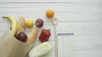 Full paper bag of food products with blank little notebook on wooden table, top view photo