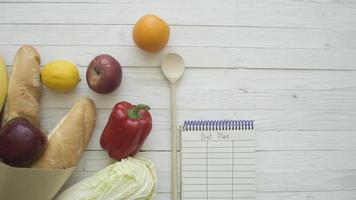 Full paper bag of food products with blank little notebook on wooden table, top view photo