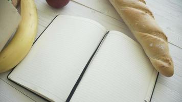 Full paper bag of food products with blank little notebook on wooden table, top view photo