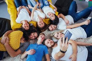 grupo de jóvenes hermosos haciendo selfie tirados en el suelo, mejores amigos niñas y niños juntos divirtiéndose, planteando un concepto de estilo de vida emocional foto