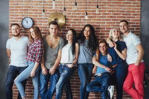 Group portrait of multi-ethnic boys and girls with colorful fashionable clothes holding friend  posing on a brick wall, Urban style people having fun, Concepts about youth  togetherness lifestyle photo