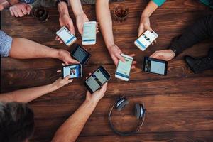 Top view hands circle using phone in cafe - Multiracial friends mobile addicted interior scene from above - Wifi connected people in bar table meeting - Concept of teamwork photo