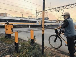 Bekasi, West Java, February 19th 2022. An old man delivering newspapers is standing waiting for the train to pass the tracks photo