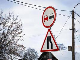 Road signs no overtaking round signa and triangle on sky background with leafless trees and snowy rooftop photo