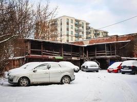 Old weathered storage shed on modern newly built building and parking with cars in winter photo