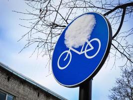 Blue round bicycle road sign with snow blob on leafless tree branches and sky background photo