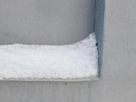 Snow layer stuck on concrete indent in gray cold wall photo