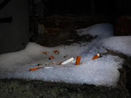 colillas de cigarrillos dejadas en la nieve escondidas en un rincón oscuro foto