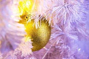 Closeup of white Christmas-tree with golden bauble hanging decorations with bokeh.