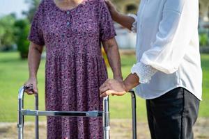 Help and care Asian senior or elderly old lady woman use walker with strong health while walking at park in happy fresh holiday. photo