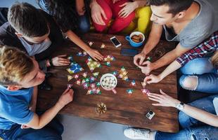 Top view creative photo of friends sitting at wooden table.  having fun while playing board game