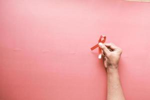 hand holding red HIV ribbon on red background top down photo