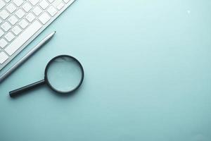 magnifying glass, pen and keyboard on blue background photo