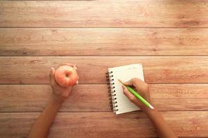 child hand writing on notepad and holding a apple photo