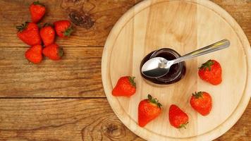 mermelada de fresa en el tarro de cristal con bayas frescas sobre fondo de madera foto