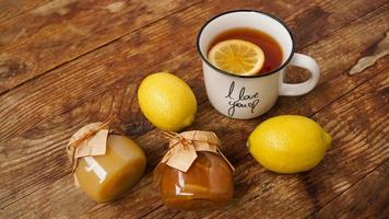 Sweet breakfast. Cup of black tea with lemon. Lemons and jars with jam photo