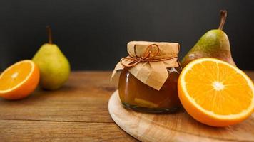 Glass jar of homemade pear and orange jam with fresh fruits on the table