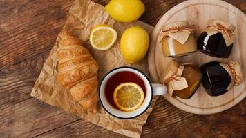 Lemon tea, home made jam, croissant on wooden table. Breakfast concept. photo