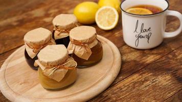 Sweet breakfast. Cup of black tea with lemon. Lemons and four jars with jam photo