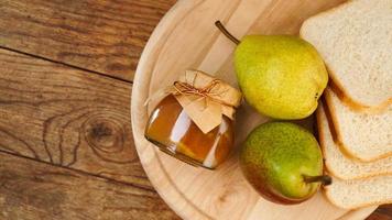 Jar of tasty pear jam with bread and fresh pear fruit on wooden table. Top view photo