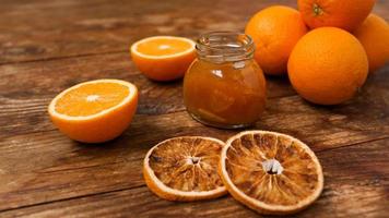 Jar of orange jam, dry oranges on wooden background from top view. photo