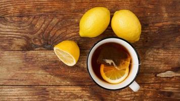 Cup of black tea with tea bag and lemons on wooden table, top view. photo
