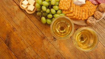 Green grapes, crackers, nuts and two glasses of white wine on wooden background photo