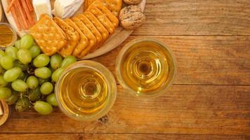 Green grapes, crackers, nuts and two glasses of white wine on wooden background photo