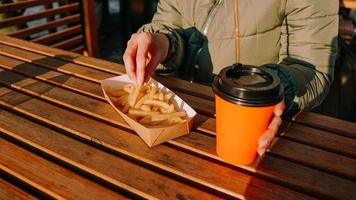 Woman eating tasty french fries and drinking tea in outdoor cafe. Close-up photo