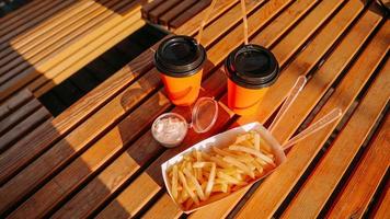 comida rápida. dos vasos de papel naranja y papas fritas con salsa en una mesa de madera foto