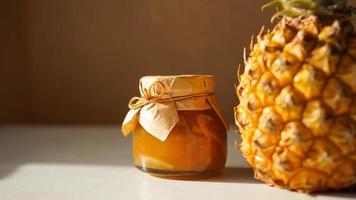 Pineapple jam in glass jar and fresh pineapple fruit with hard shadows photo