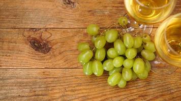 A branch of green grapes and two glasses of white wine on a wooden background photo