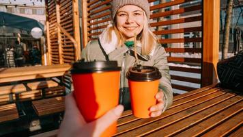 Two friends clink paper cups with mulled wine or hot tea on a sunny winter day photo
