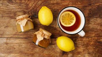Sweet breakfast. Cup of black tea with lemon. Lemons and jars with jam photo