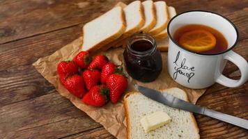 White cup of black tea with lemon. Sandwiches with strawberry and jam jar