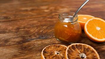 Jar of orange jam, dry oranges on wooden background from top view. photo