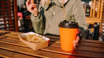 Woman eating tasty french fries and drinking tea in outdoor cafe. Close-up photo