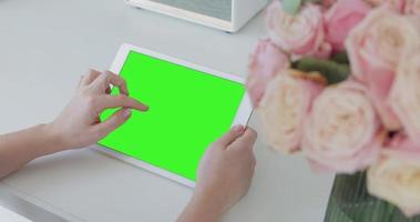 Woman using white tablet device computer with green screen touchscreen. View from behind woman sitting in the living room and holding the tablet device with green screen horizontally video