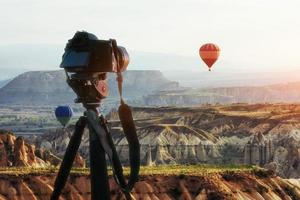 globo aerostático volando sobre el paisaje rocoso en turquía. cámara dslr en un trípode en primer plano foto