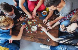 Top view creative photo of friends sitting at wooden table.  having fun while playing board game