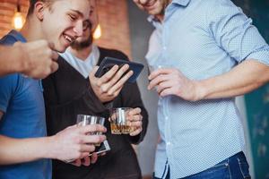 Cheerful old friends communicate with each other and phone watch,  glasses of whiskey in pub. Concept  entertainment  lifestyle. Wifi connected people in bar table meeting photo