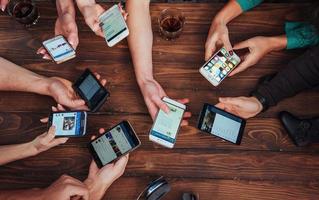 Top view hands circle using phone in cafe - Multiracial friends mobile addicted interior scene from above - Wifi connected people in bar table meeting - Concept of teamwork photo