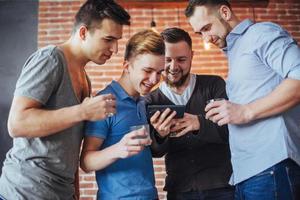 Cheerful old friends communicate with each other and phone watch,  glasses of whiskey in pub. Concept  entertainment  lifestyle. Wifi connected people in bar table meeting photo