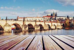 view of the Charles Bridge which crosses the River Vltava and wooden pier in foreground photo