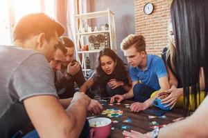Group of creative friends sitting at wooden table. People having fun while playing board game photo