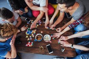 Top view creative photo of friends sitting at wooden table.  having fun while playing board game